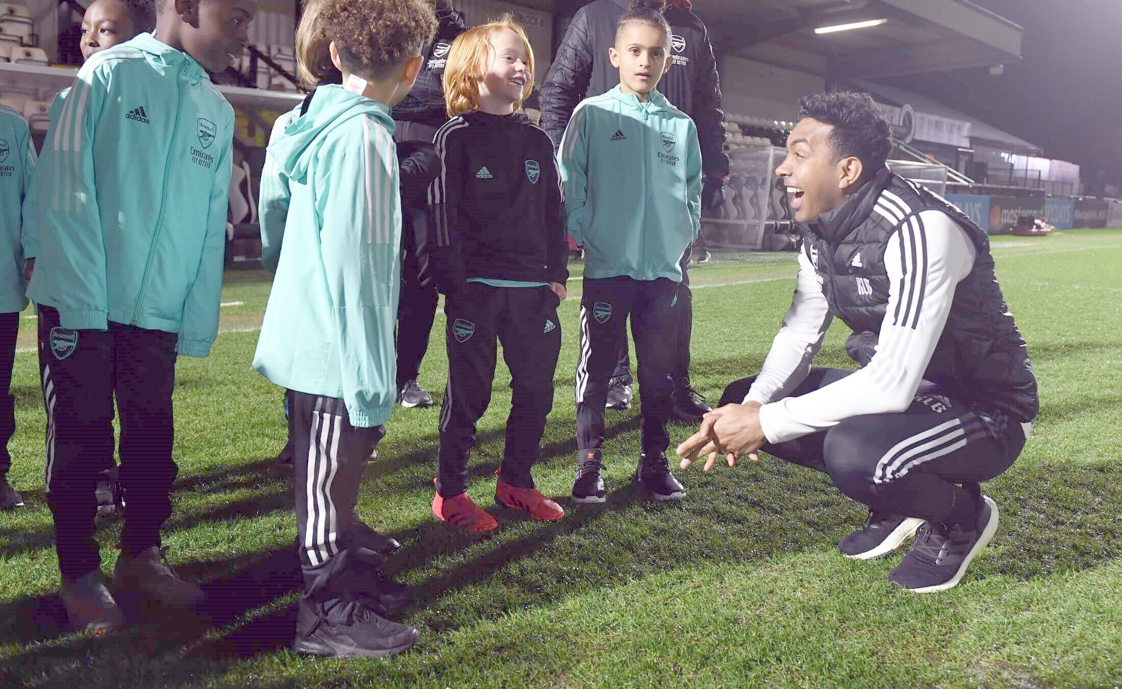A coach squats down to talk to a group of young footballers inside a football stadium