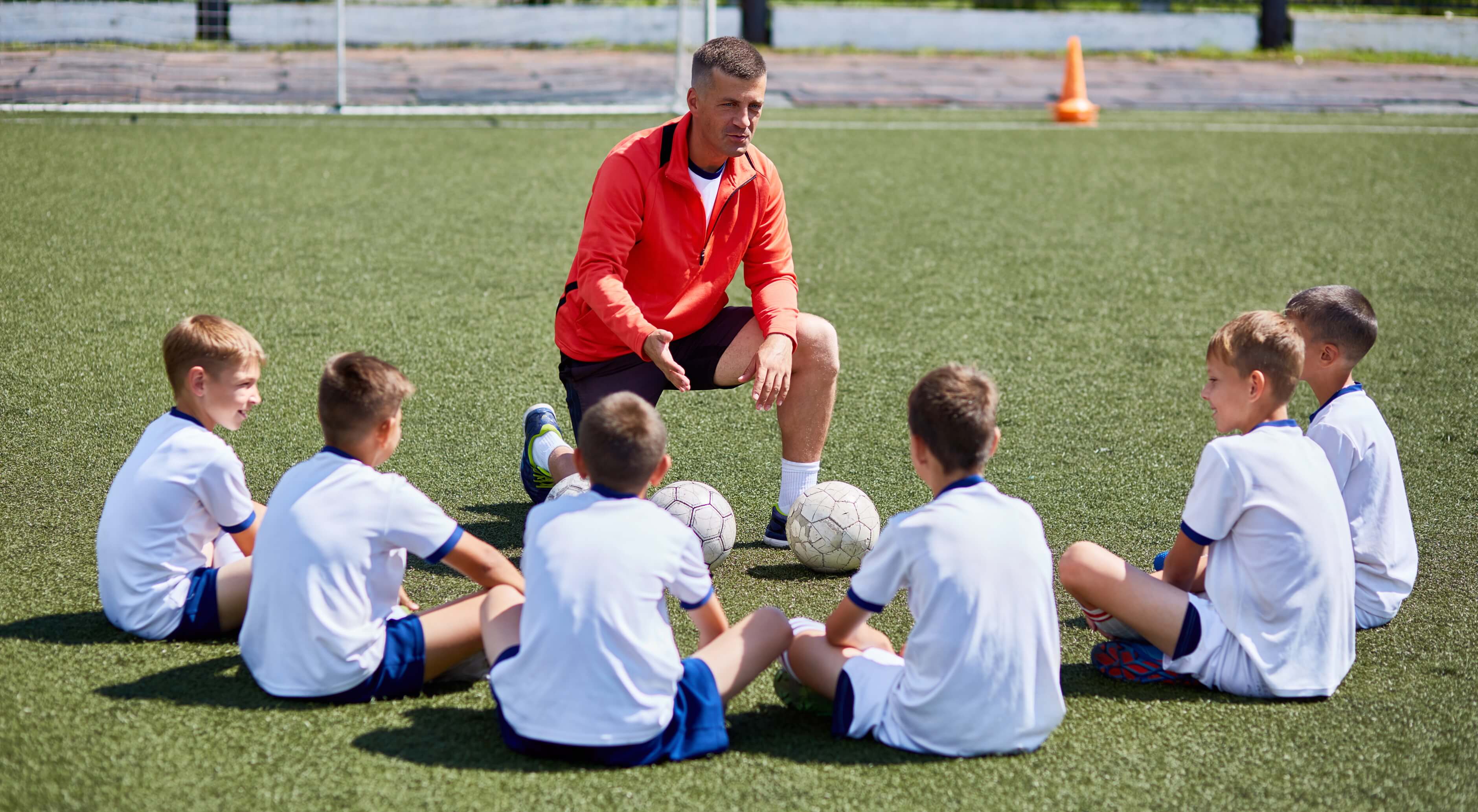Sports coach talking to children sat in a semicircle