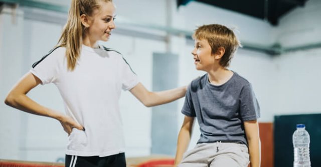 Coach talking to participant who is sat on gymnastics equipment