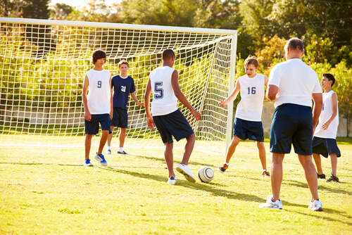 Teenage boys playing football on a football pitch with their coach