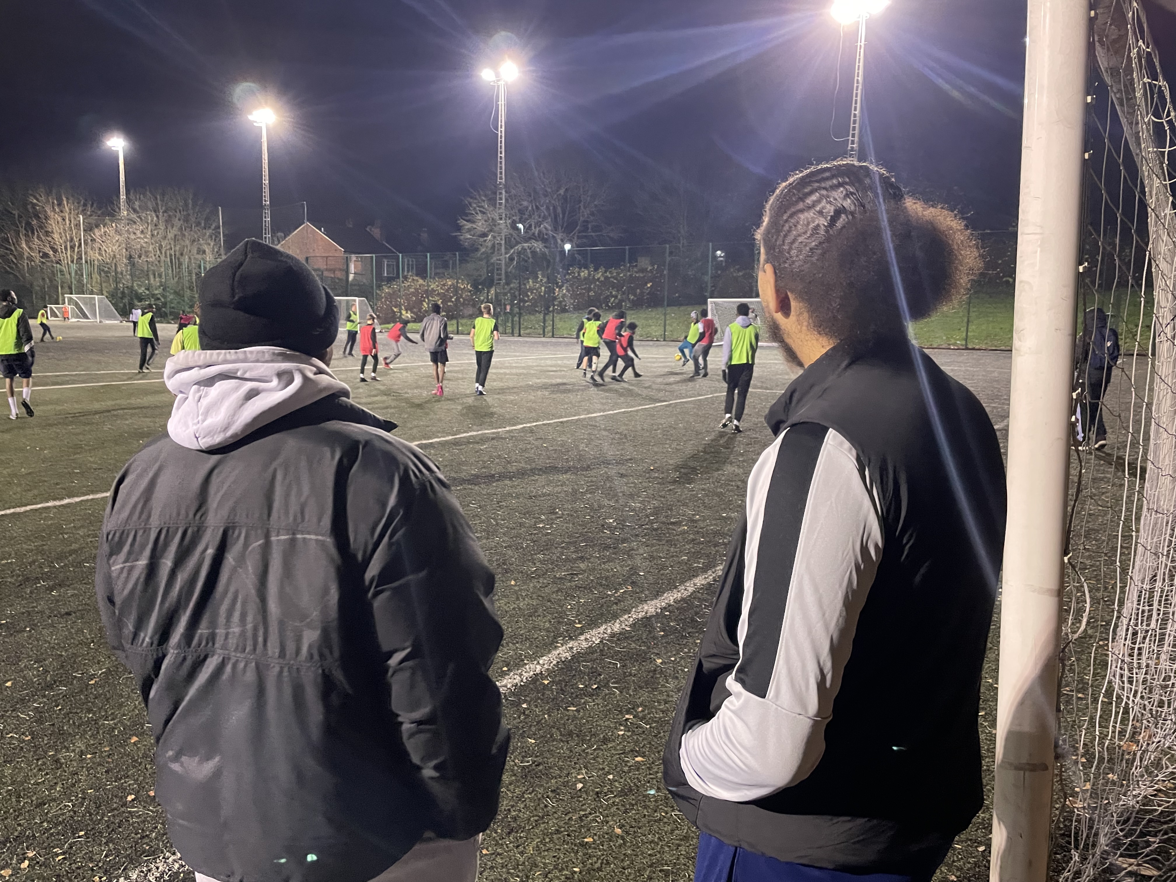 Two coaches overlooking a football training session.