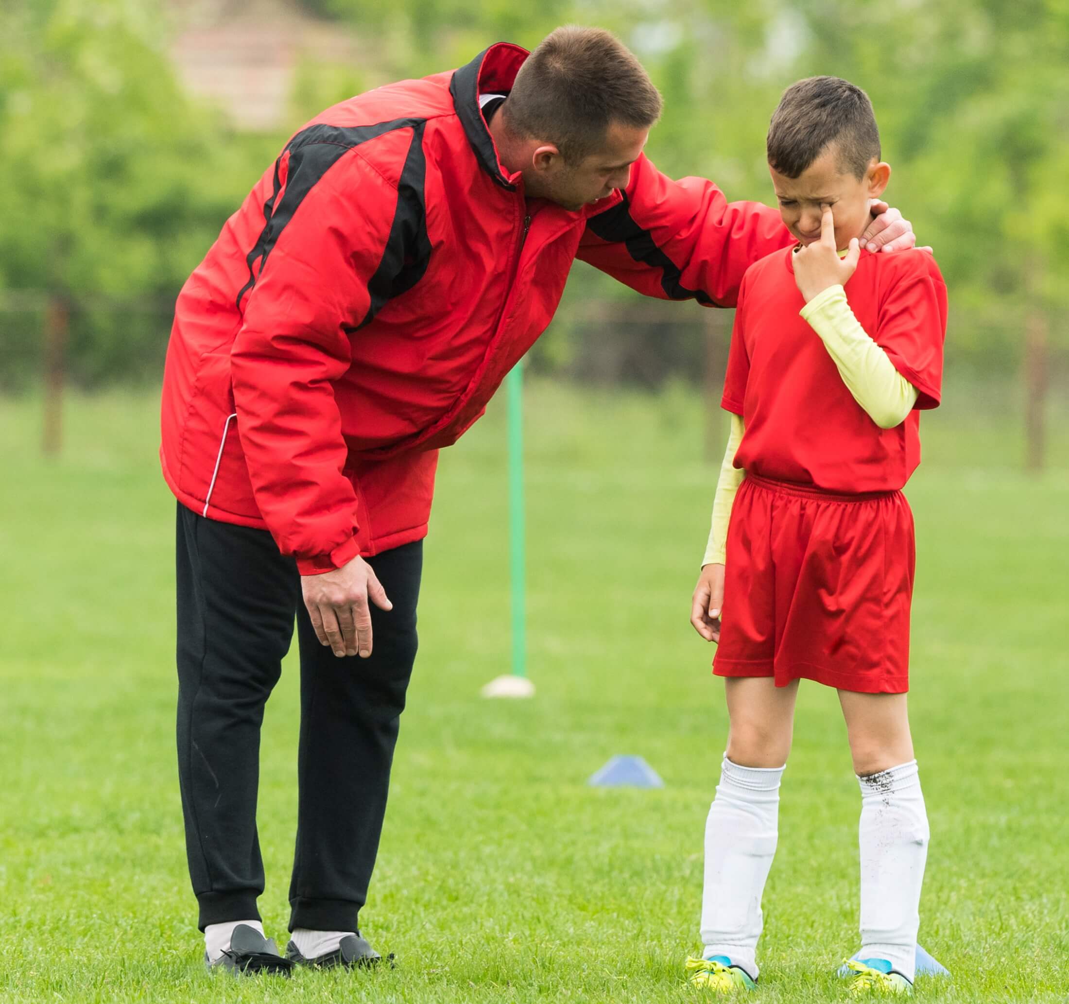 Coach leans in to offer support to a young footballer who is crying