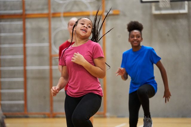 A young girl smiling and having fun as she does knees up exercises in a school hall