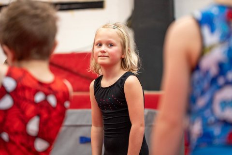 Young girl in a black leotard is taking part in a gymnastics session. 