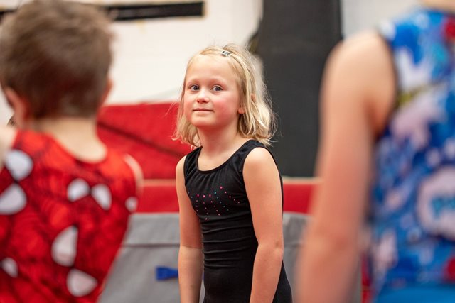 Young girl in a black leotard is taking part in a gymnastics session. 