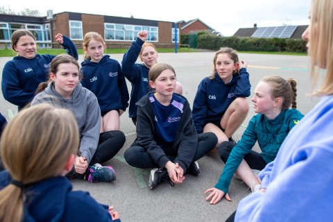A group of young girls are sat on the playground talking to their female coach. 