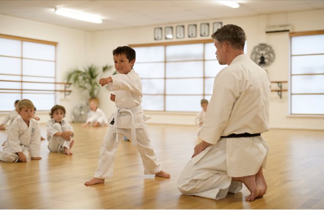 Young karate student delivers a straight punch with his left arm, watched by his coach