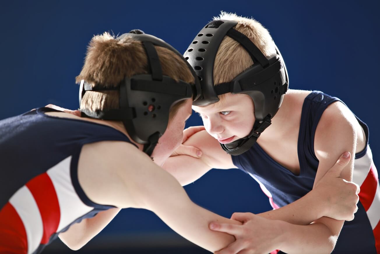 Two young teenage boys in blue, red and white wrestling vests are in a wrestling grip.