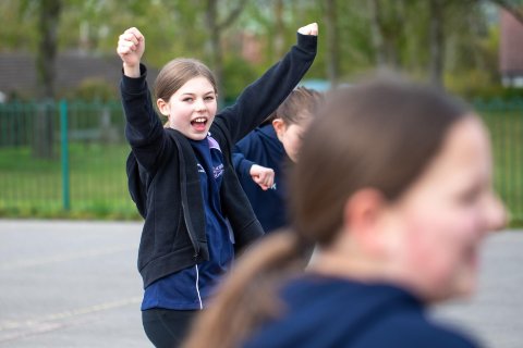 Young girl celebrates a goal with both hands in the air. 