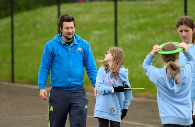 A smiling coach watches a young girl turn with an ultimate frisbee, both with joy on their faces