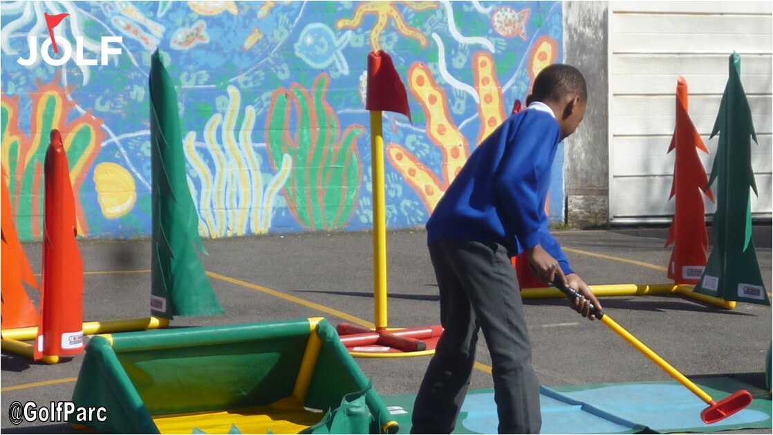 Young boy in a blue jumper is playing a round of indoor golf 