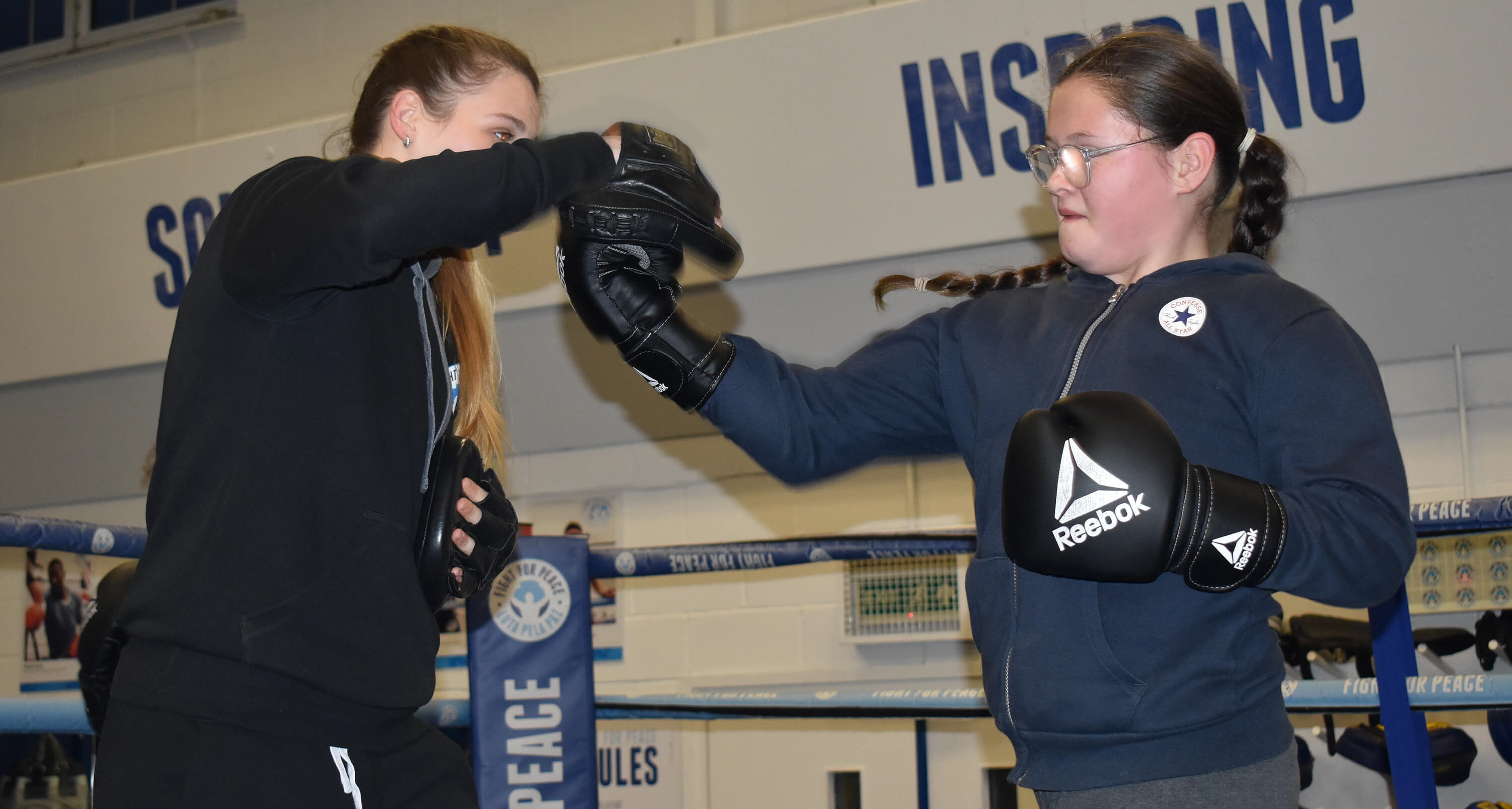 A young boxer delivers an uppercut on the pads during training with their coach in the ring