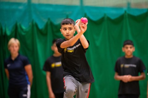 A bowler runs up to the crease ready to bowl holding a pink cricket ball