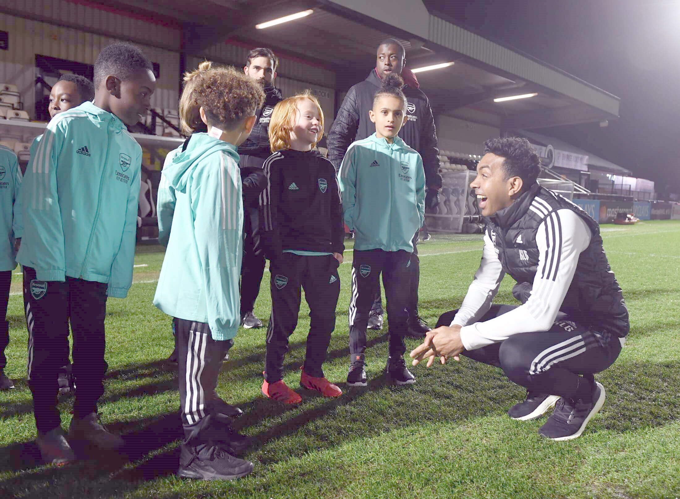 A coach squats down to talk to a group of young footballers inside a football stadium