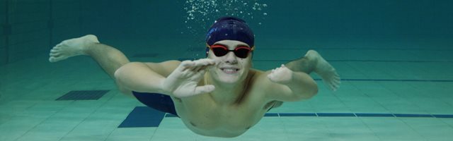 Young person swimming underwater, waving at the camera