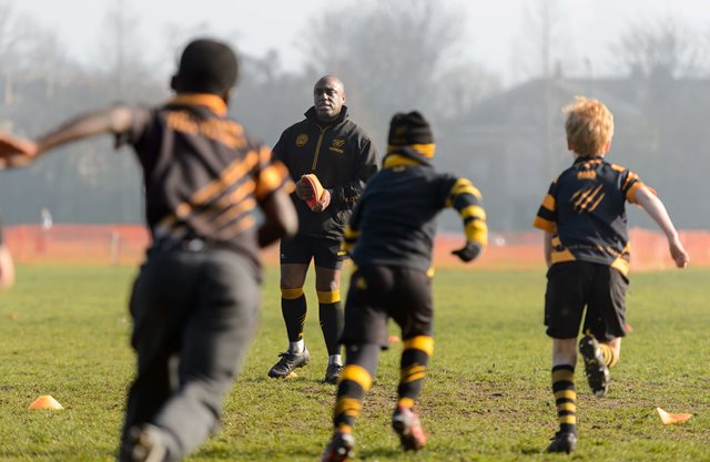 A children's rugby union coach watches his participants during an outdoor training session 
