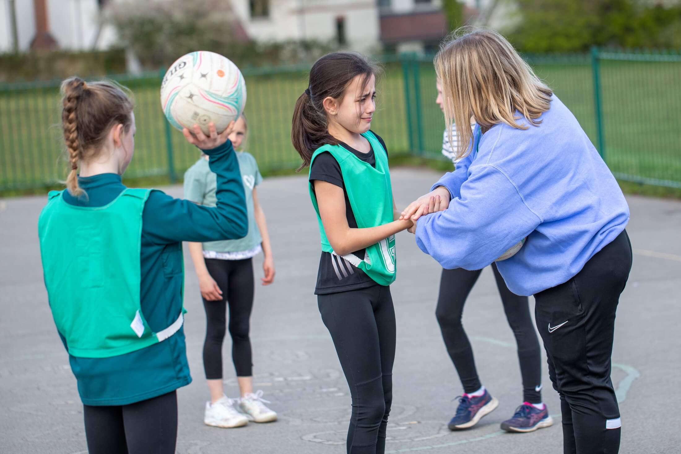 Coach helps a young girl who is visibly upset after hurting her hand playing netball