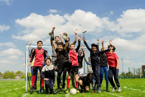 Group of young boys celebrate jumping up together in front of the goal