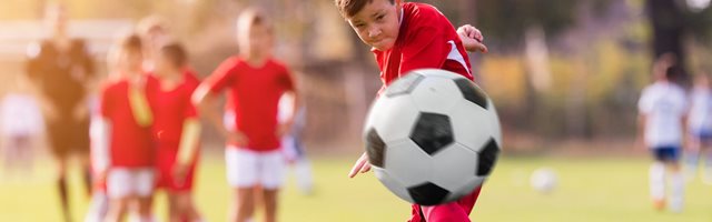 Boy in red and white football strip kicks a black and white football towards the camera
