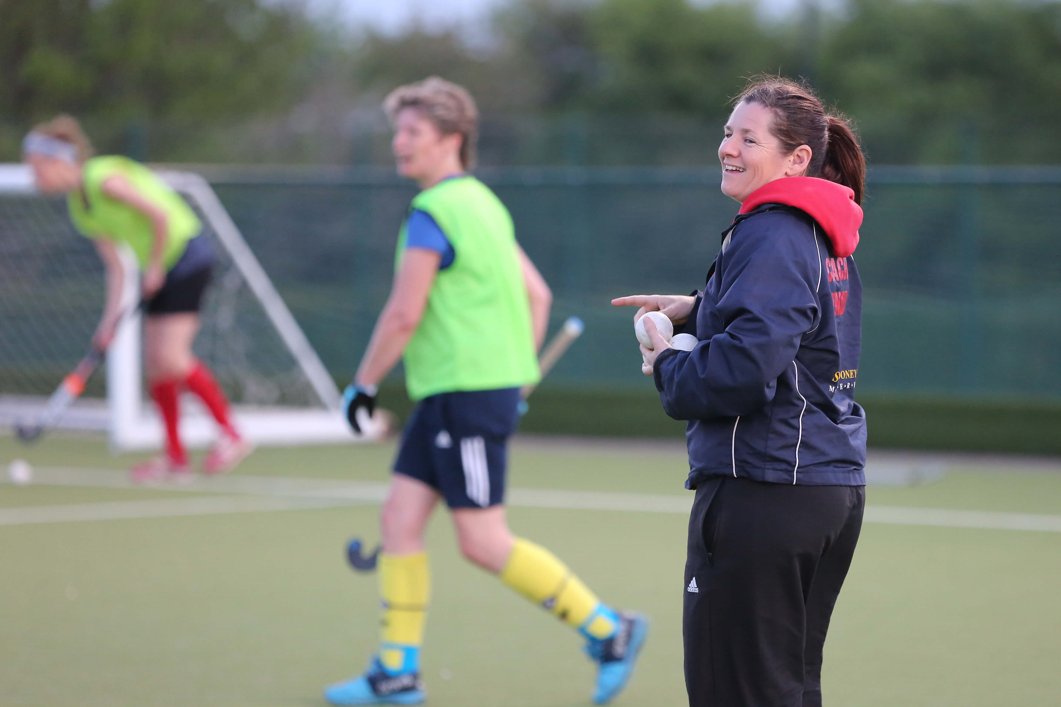 Smiling hockey coach watches a training session on an outdoor pitch