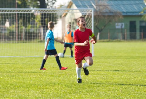 Boy wearing red football kit celebrating after scoring a goal