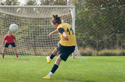 Teen girl kicks football at a goal on a football field