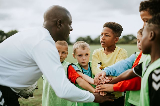 Football coach with kids in a huddle doing a high five