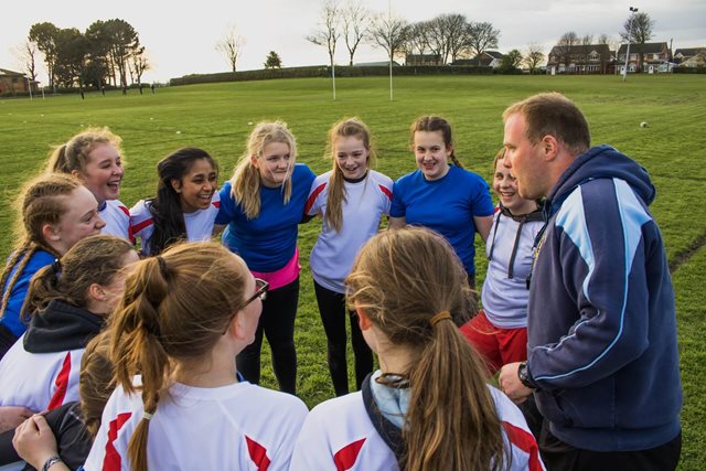 Group of rugby playing girls huddle around as their coach speaks to them