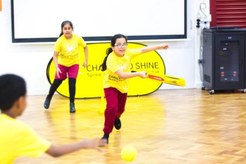 A girl races down the crease after hitting the ball as a fielder attempts to stop the ball