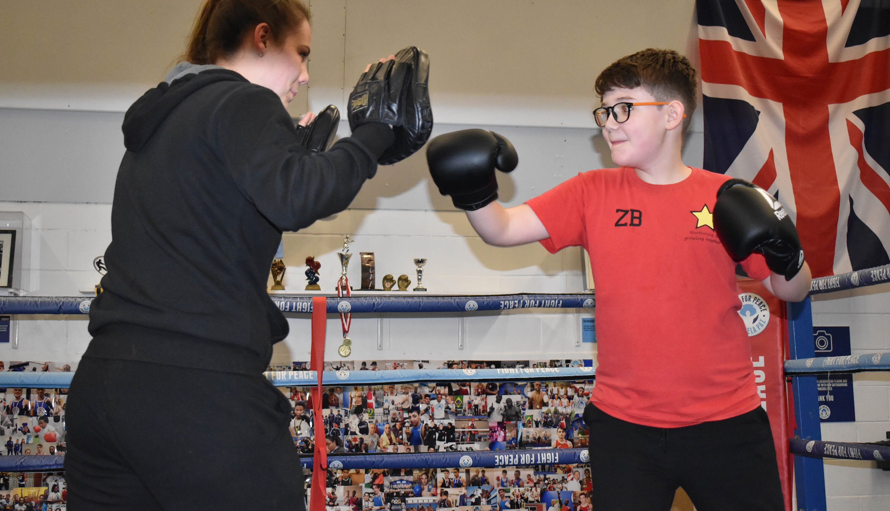 Young boxer wearing a red t-shirt delivers a right hand punch to the pads during training in the ring