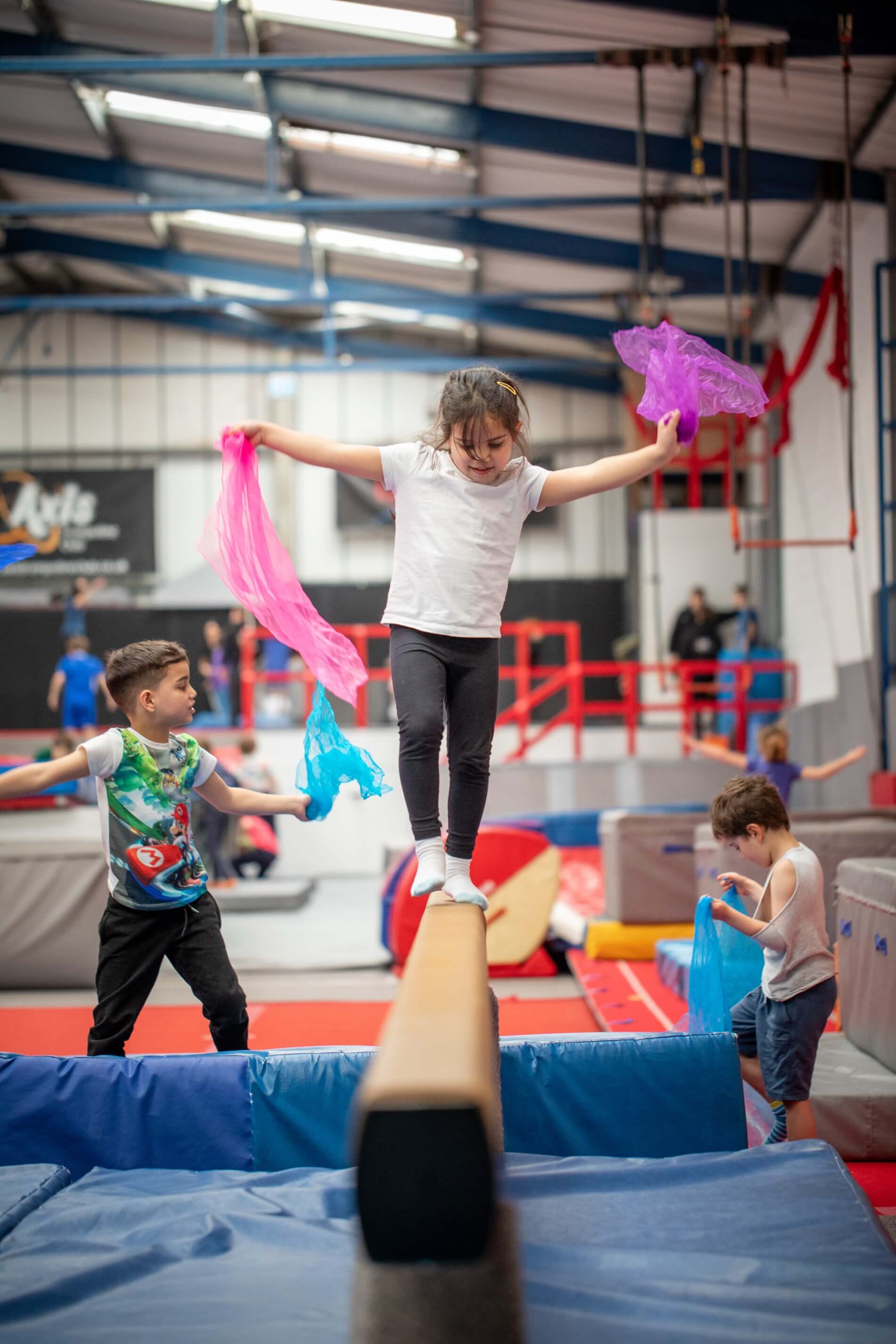 Young girl holding two pink scarves is balancing on a bar. 