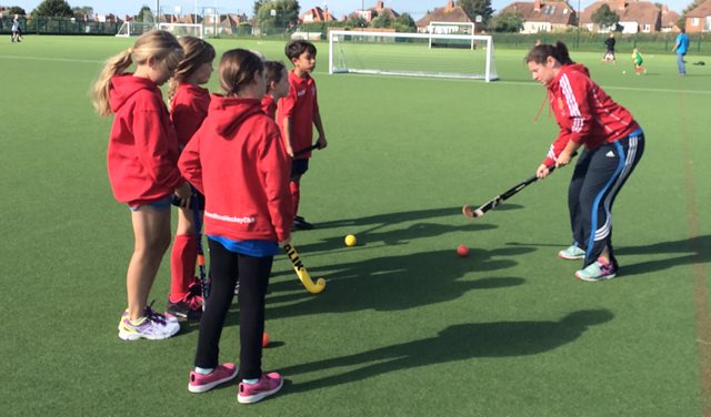Hockey coach demonstrates a skill to her group of players on the pitch