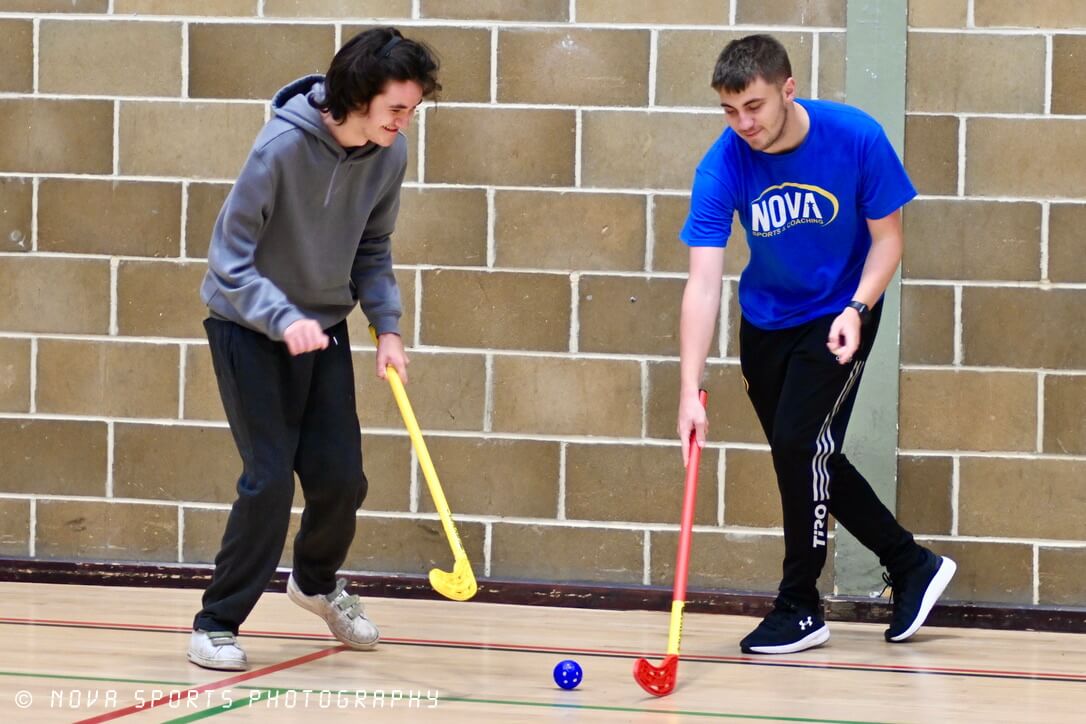 Two smiling participants playing hockey in a sports hall
