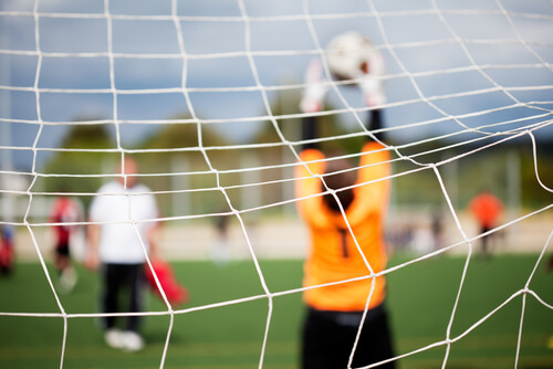 Goalie in front of a football net saving a goal