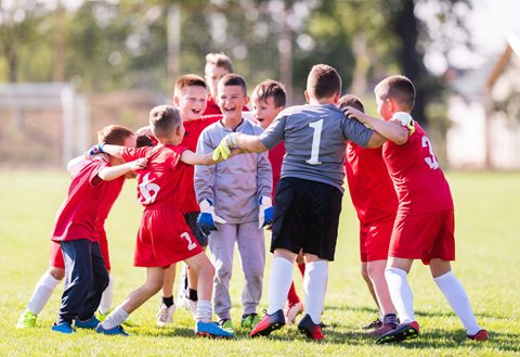 A group of happy smiling young boys come together for a group hug during football training