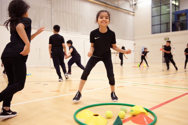 A young girl celebrates amidst a fun and engaging setup of cones and bean bags in a school hall