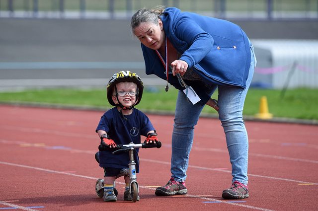 Young disabled boy learning to ride a bike on an outdoor track with coach
