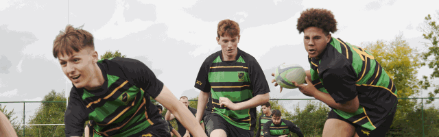 Three boys are running across a rugby pitch passing the ball