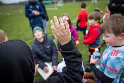 A child raises their hand in the air as the group chat to their coach