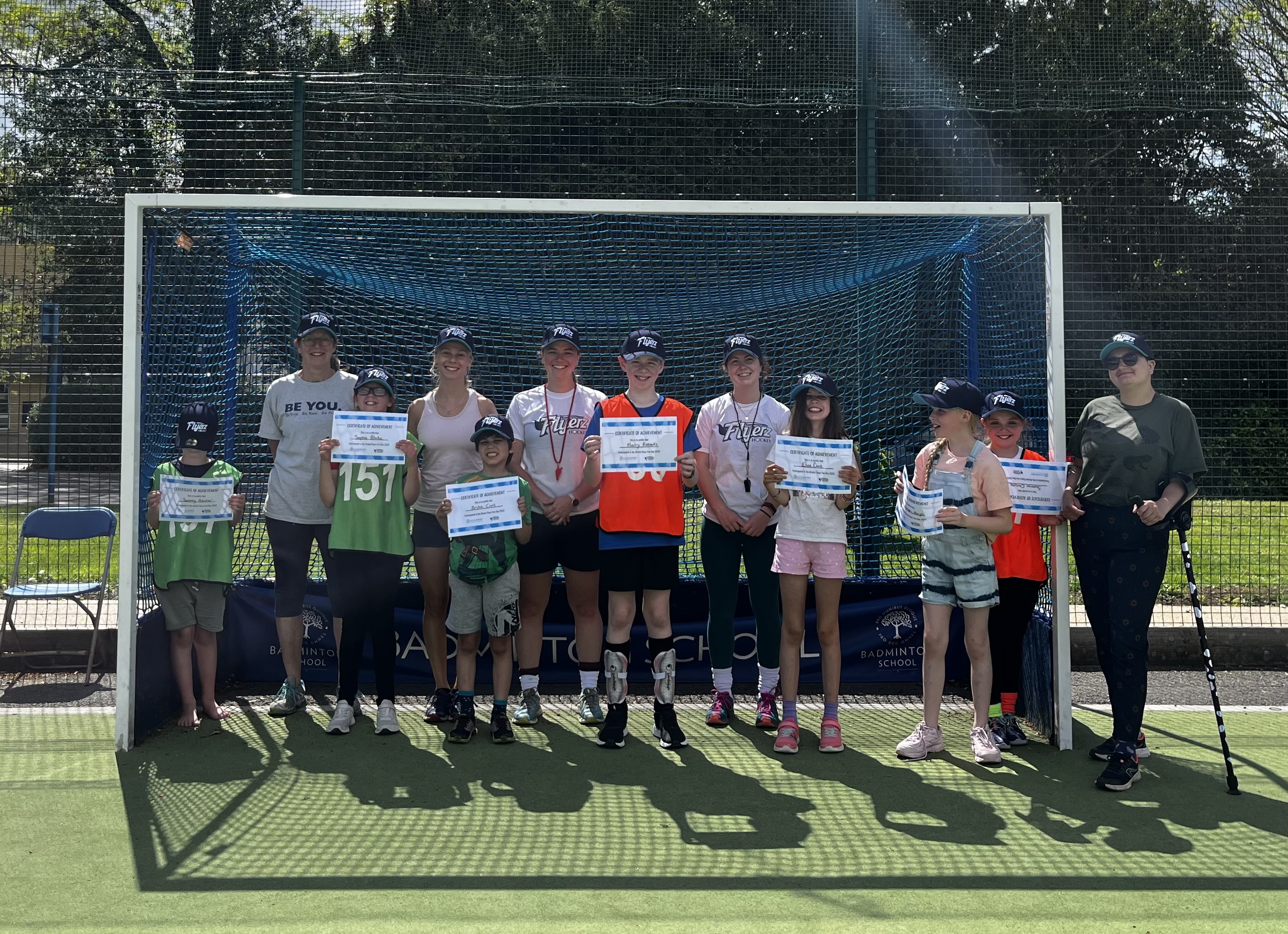 Smiling group standing in front of goal posts holding certificates