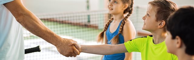 Tennis coach shakes smiling childs hand