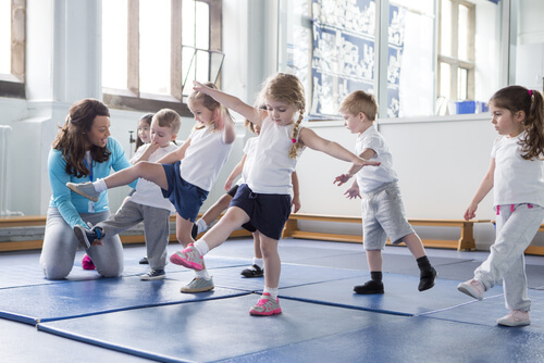 Gymnastics class with small children balancing on one foot on gym mats in a sports hall