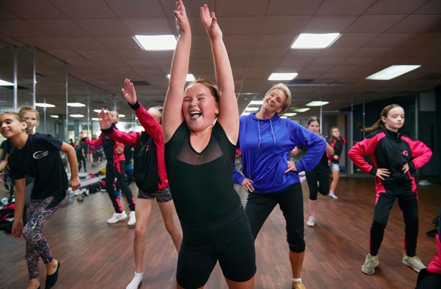 Young girl smiling and dancing in a class with other children in the background