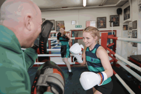 Girl in a striped green and black vest is doing some boxing padwork with her male trainer