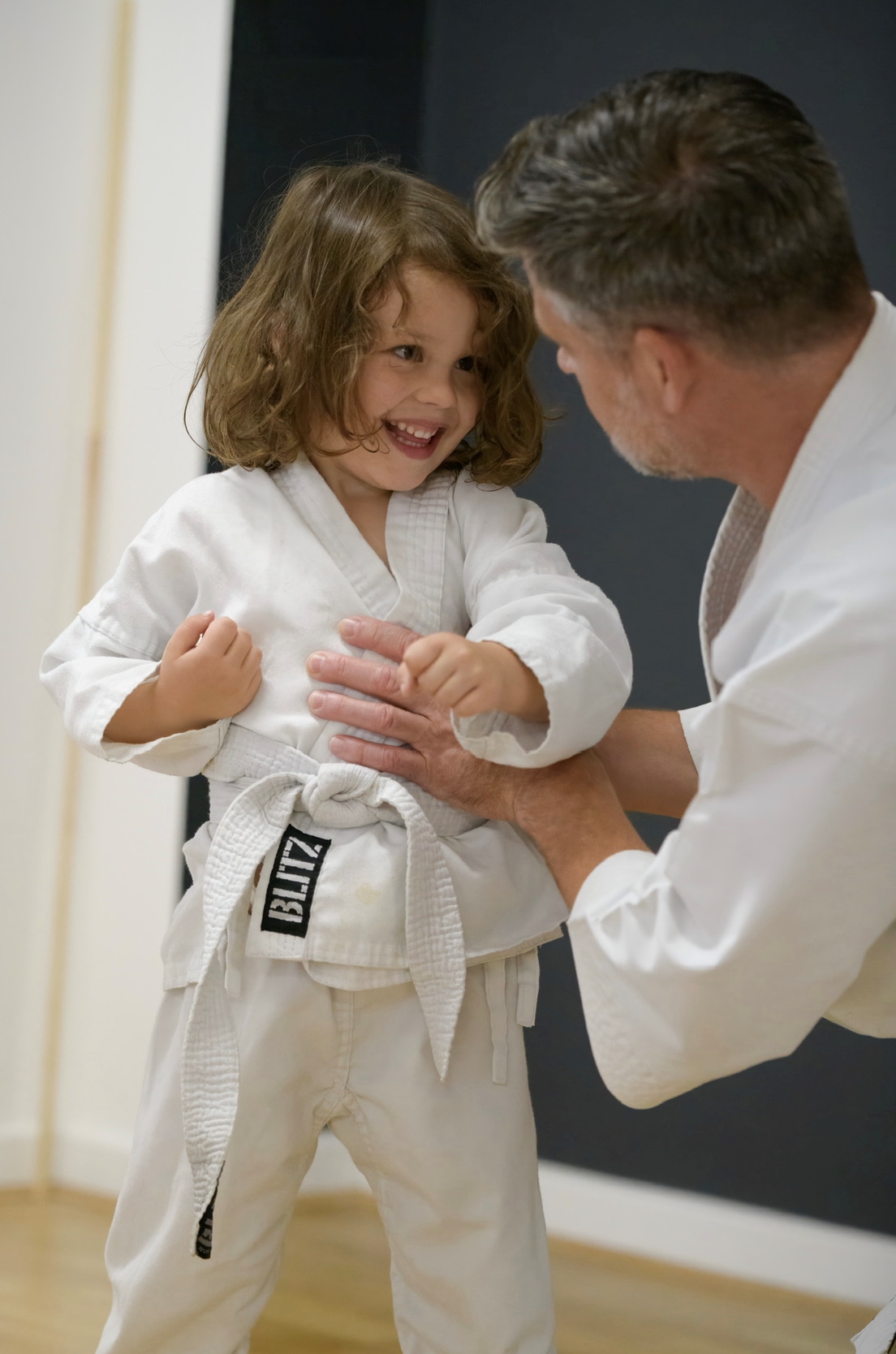 A young karate student smiles as their coach bends down to talk to them at eye level 
