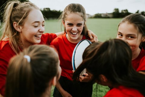 Group of girls laughing, one holding rugby ball