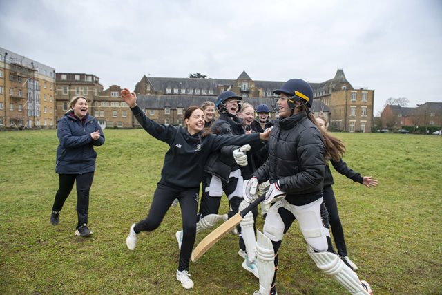 Coach-and-groups-of-girls-on-a-cricket-field-celebrating-a-shot-from-the-batter