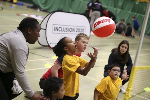 Group of children playing volleyball in a gym with their coach