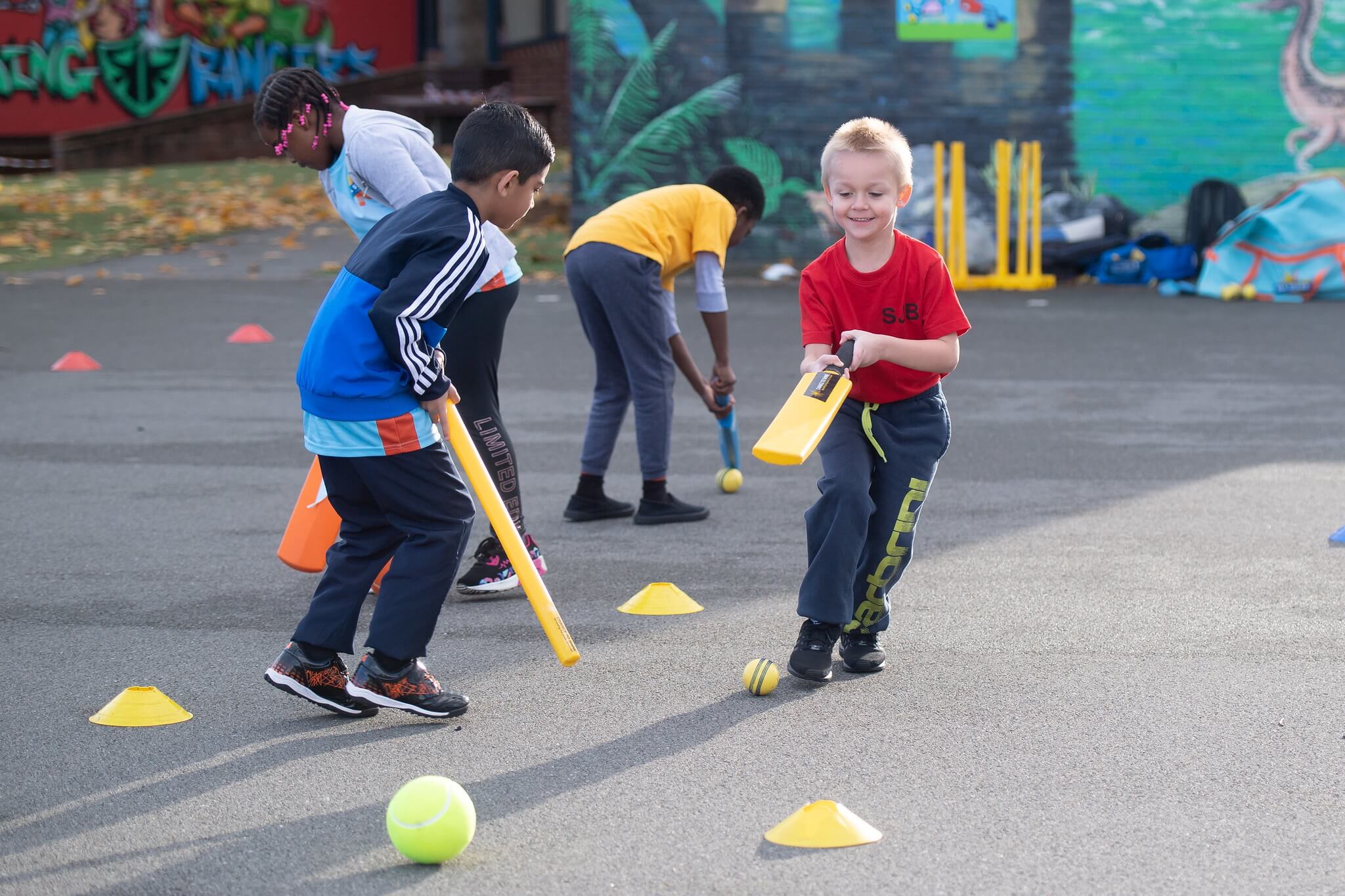 Children practise their dribbling skills using cricket bats and stumps to move the ball 