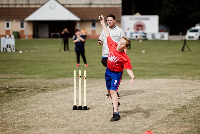 Young cricketer bowls on the square as his coach watches on 